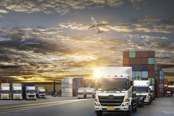 mehrere LKWs und große Container mit Sonnenaufgang im Hintergrund